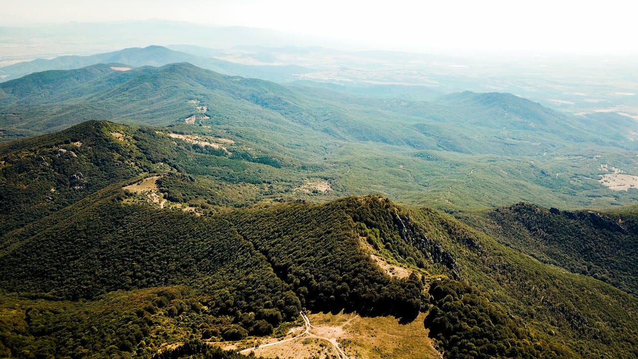 Breathtaking aerial view of lush green mountains and valleys under a clear summer sky.