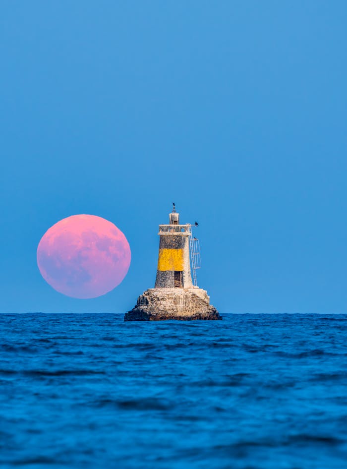 A stunning view of a lighthouse with the full moon rising over the Black Sea in Pomorie, Bulgaria.
